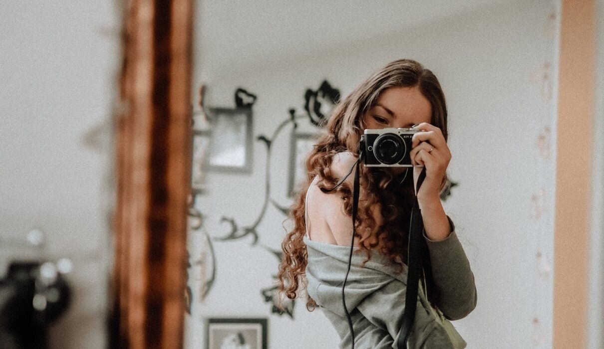 Woman taking a selfie in front of her mirror with a camera