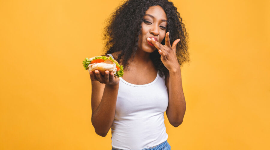 Woman eating burger behind a yellow wall