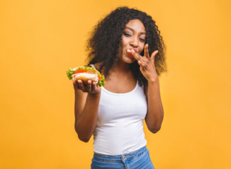 Woman eating burger behind a yellow wall