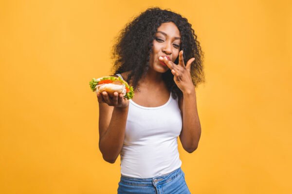 Woman eating burger behind a yellow wall