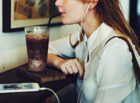 Woman drinking cold coffee in a cafe, listening to music on her iphone