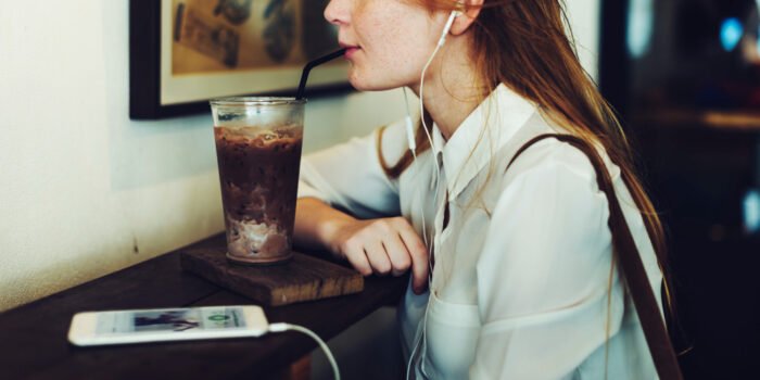 Woman drinking cold coffee in a cafe, listening to music on her iphone