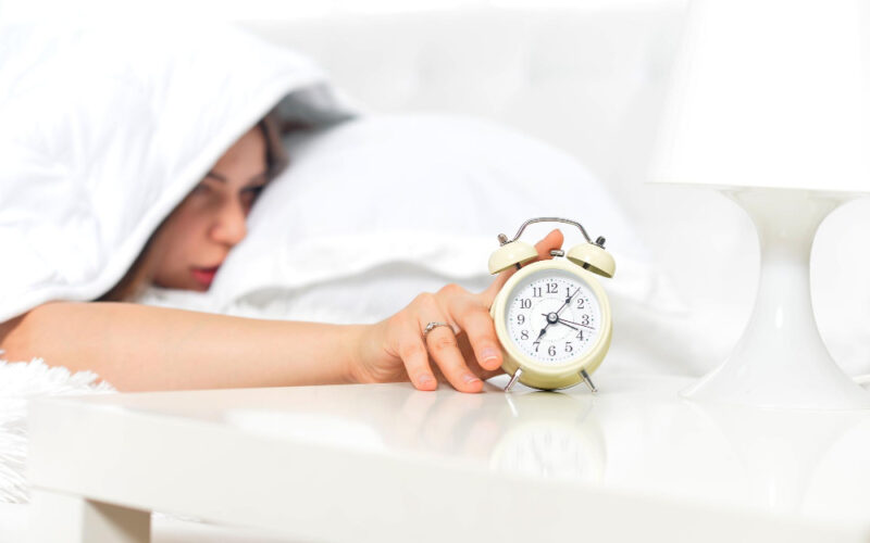 Woman sleepily trying to turn off her alarm clock