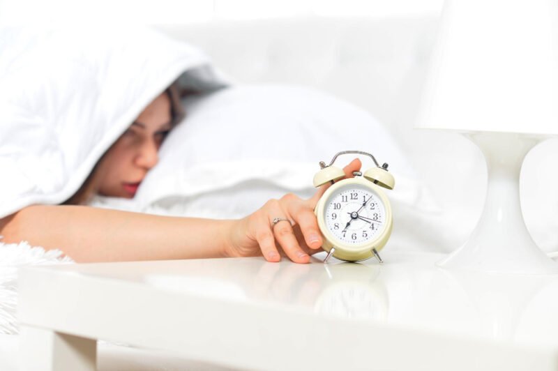 Woman sleepily trying to turn off her alarm clock