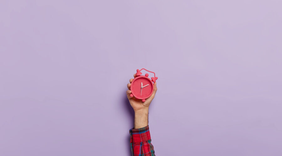 Person Holding up a red clock against purple background