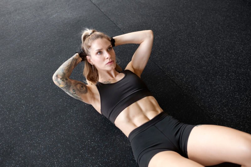 Woman with tattoos on the gym floor doing ab crunches