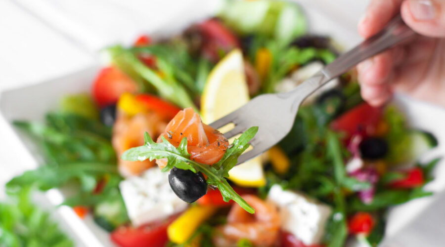 A fork with smoked salmon and olive from a salad below