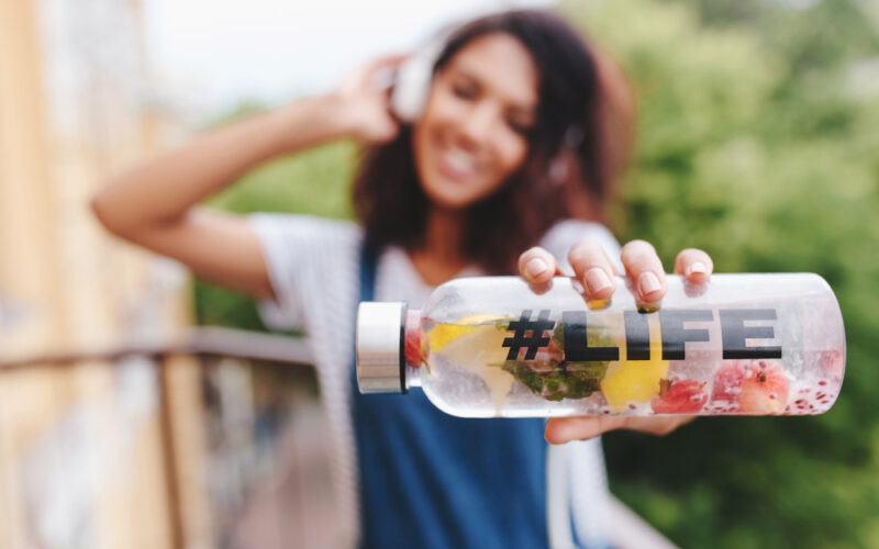 Young woman blurred in the background, holding a bottle of water with fruit and life written on it