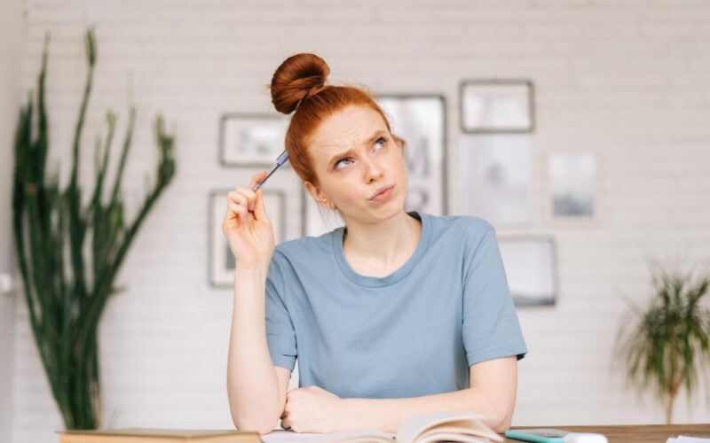 Redhead woman at home, studying and contemplating her material with a pencil directed to her brain
