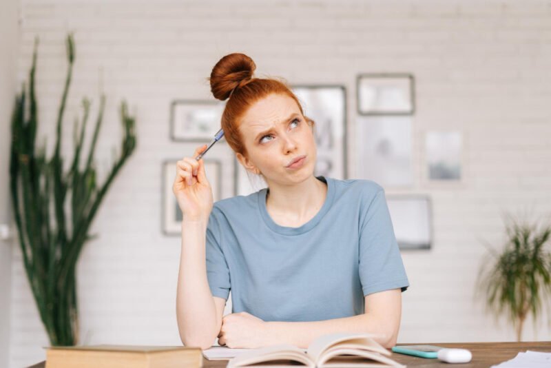 Redhead woman at home, studying and contemplating her material with a pencil directed to her brain