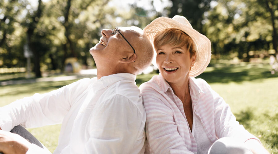 Older woman and man sitting down in a park on a sunny day smiling and laughing