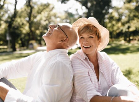 Older woman and man sitting down in a park on a sunny day smiling and laughing