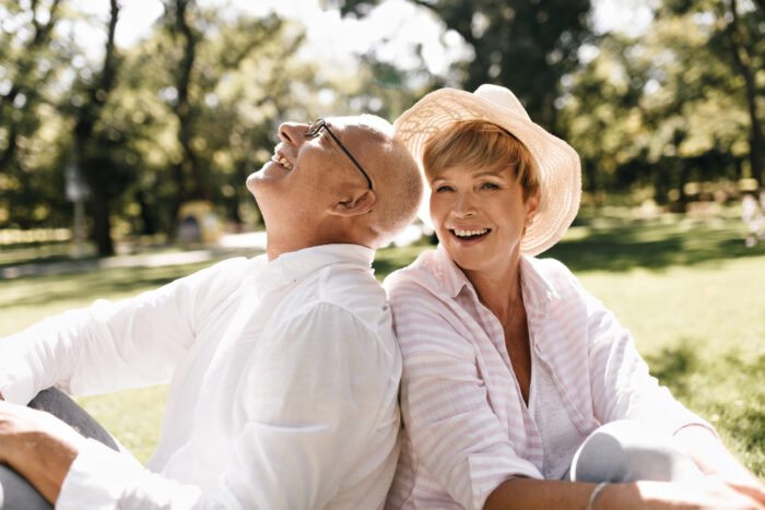Older woman and man sitting down in a park on a sunny day smiling and laughing