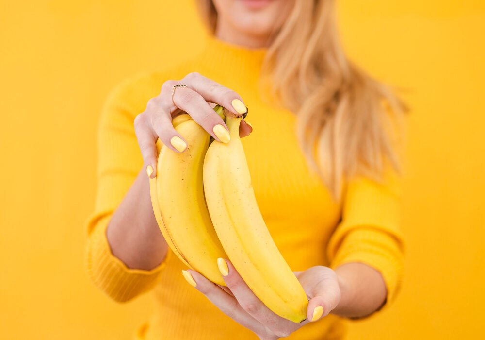Woman holding a bunch of bananas with a yellow jumper and background