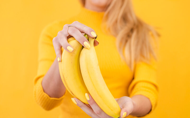 Woman holding a bunch of bananas with a yellow jumper and background
