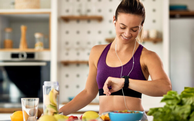 happy-athletic-woman-checking-time-her-wristwatch-while-preparing-fruit-smoothie-kitchen
