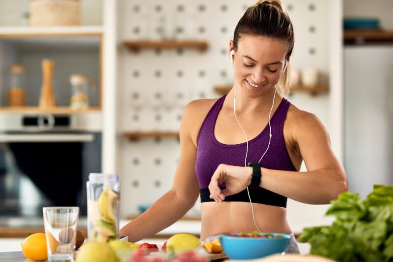 happy-athletic-woman-checking-time-her-wristwatch-while-preparing-fruit-smoothie-kitchen
