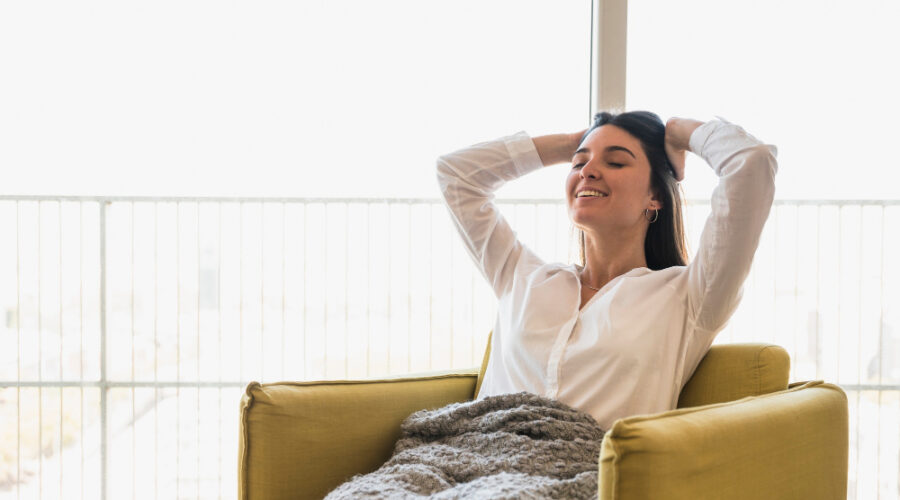 smiling-portrait-young-woman-with-her-hands-head-sitting-armchair