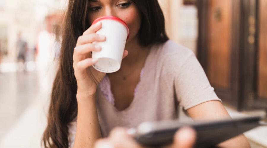 Woman drinking her cup of coffee while reading on her tablet